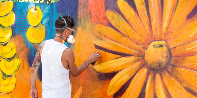 Male graffiti artist using spray for a large mural with floral elements